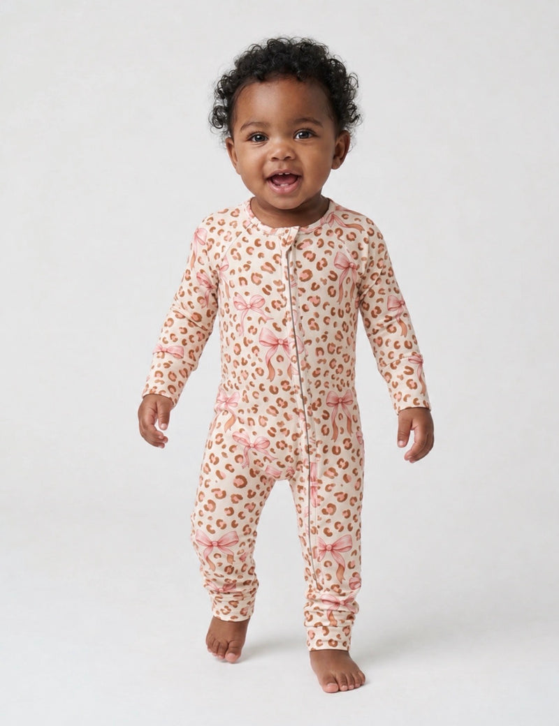 A smiling baby girl wearing a long-sleeved romper with a pink leopard print and bow pattern.